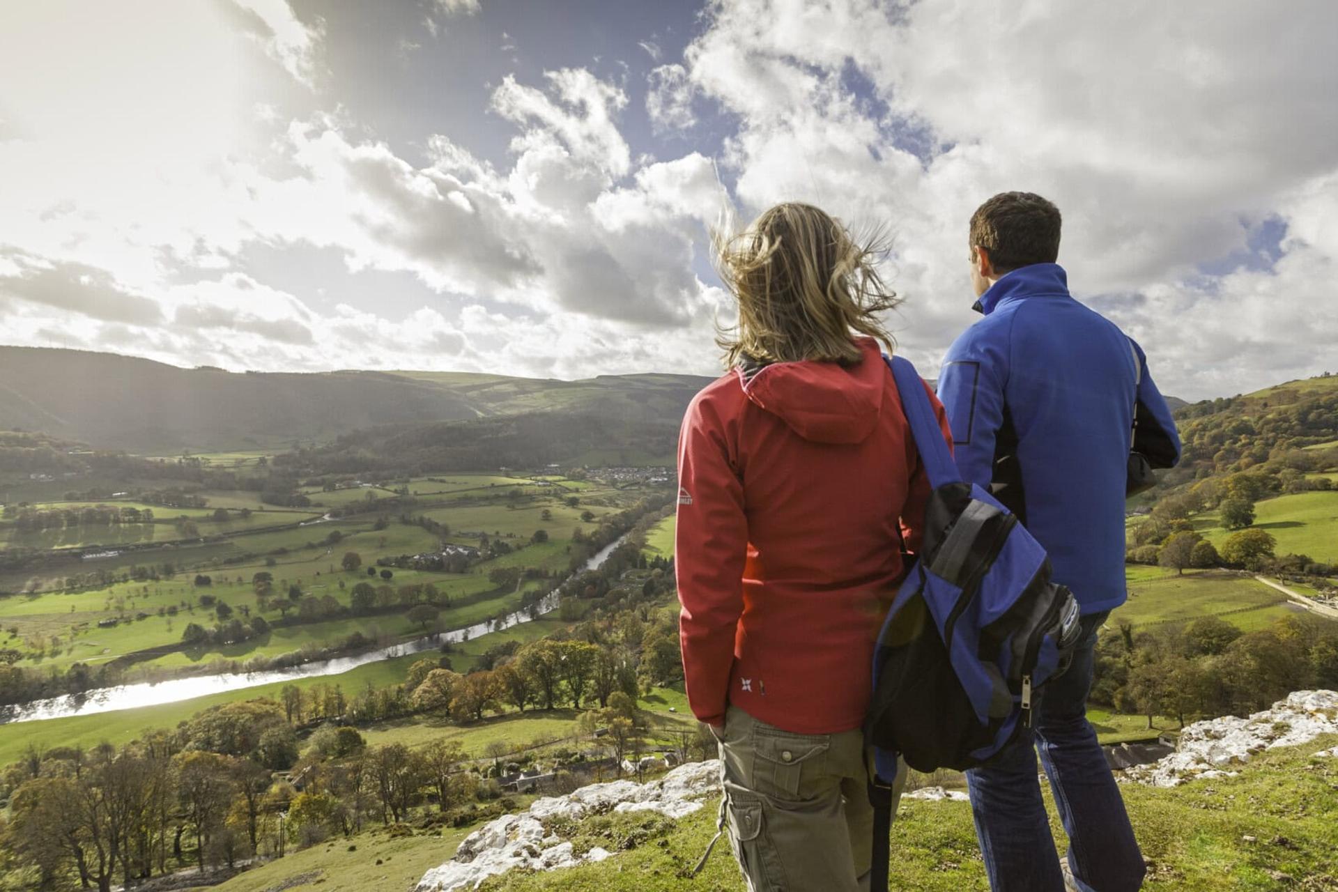 Two people looking out across a countryside valley, with green hills and a river.