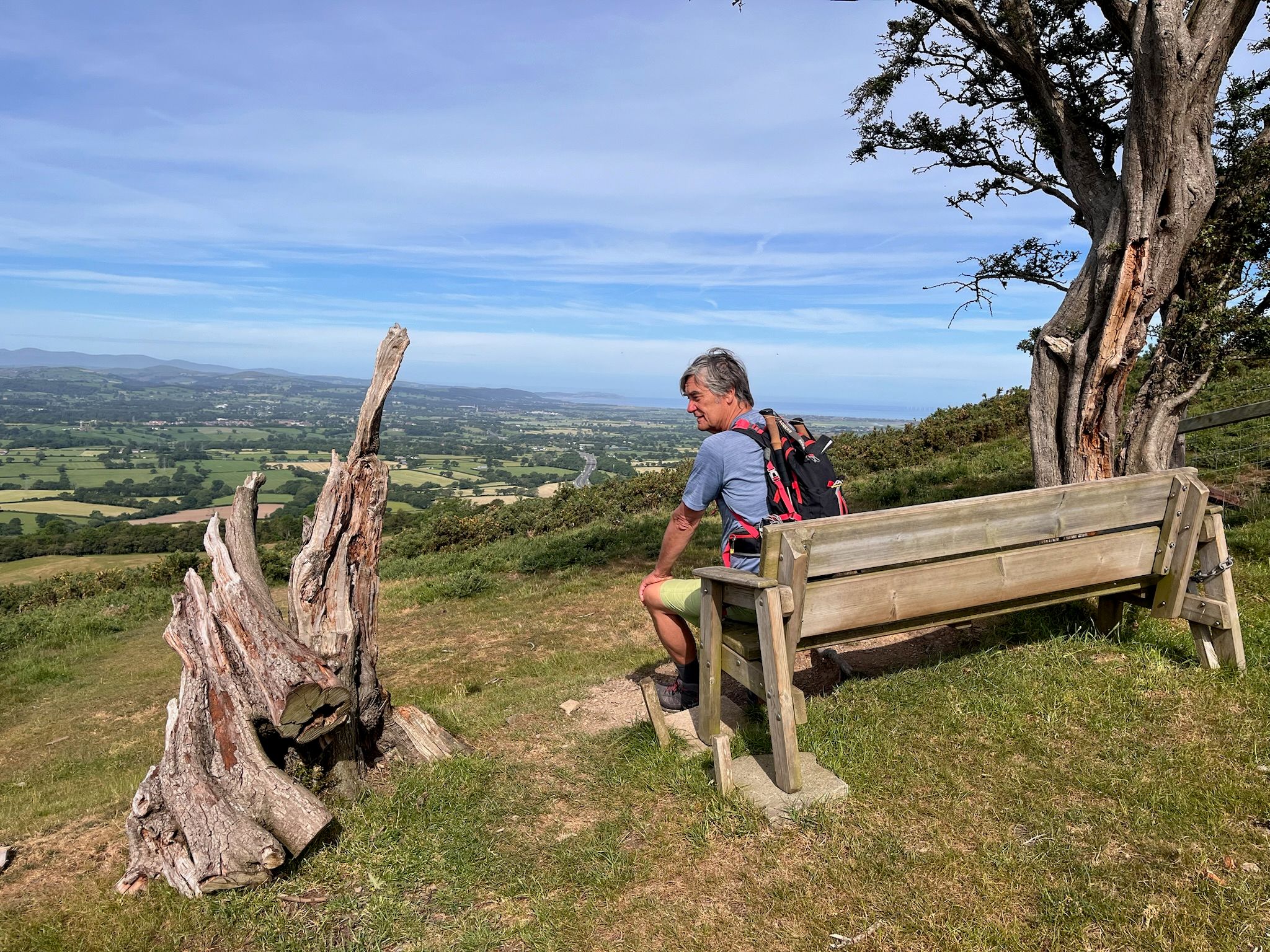 Walker resting on a bench with wide countryside and coast views during a self-guided walk.