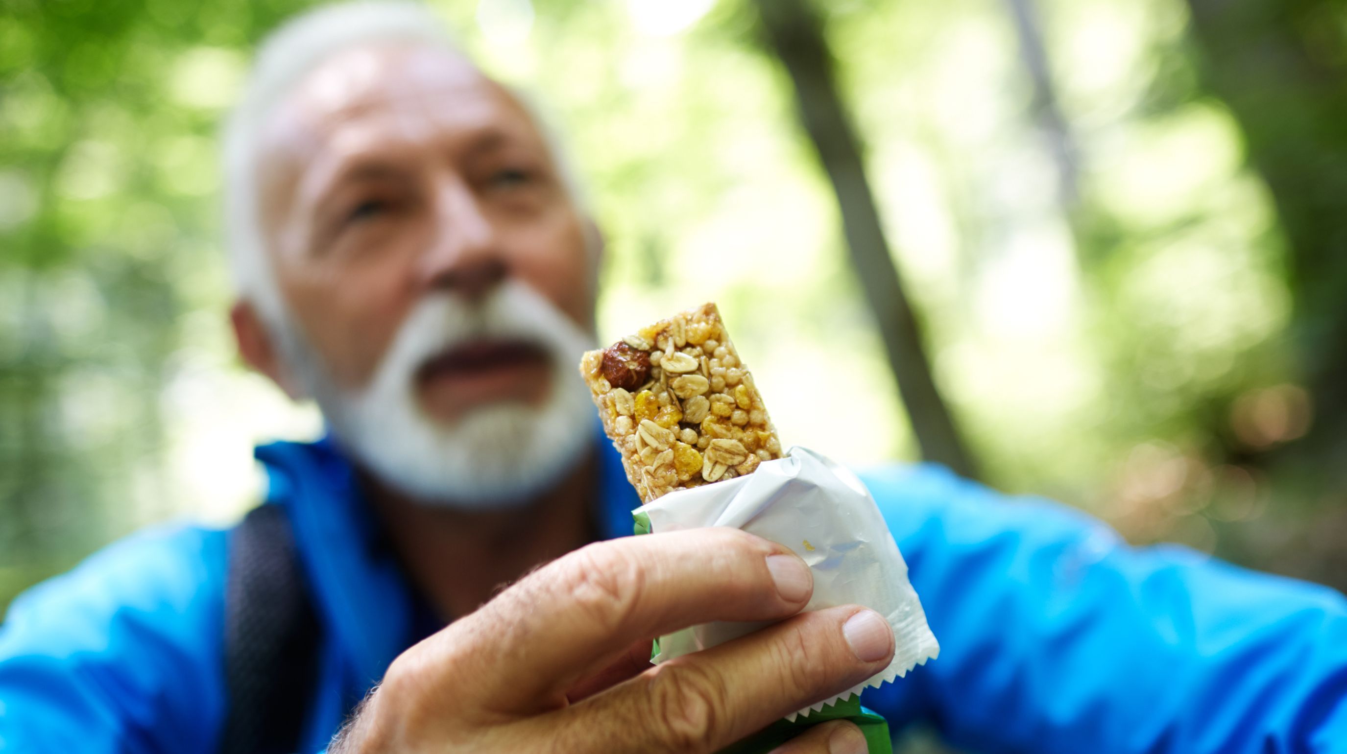 A person holding a granola bar outdoors in a forest.