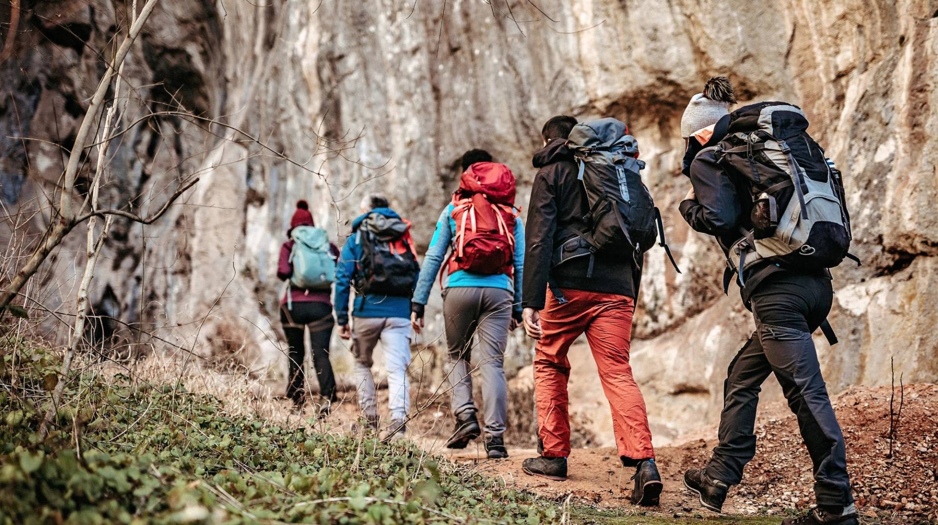 A group of hikers with large backpacks walk along a rocky path surrounded by sparse vegetation.