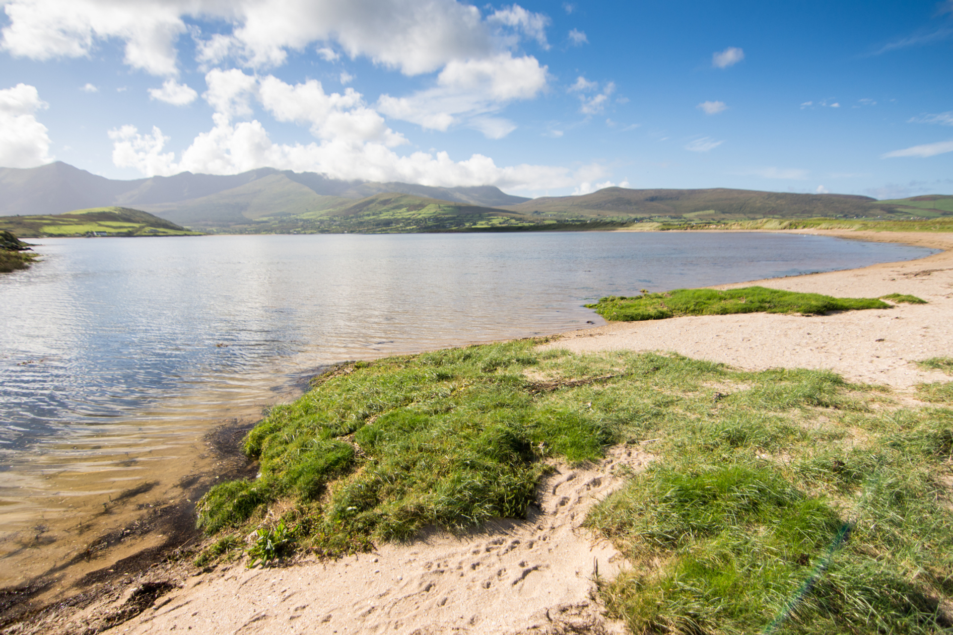 Sandy shoreline and calm estuary waters near Cloghane with mountains beyond.