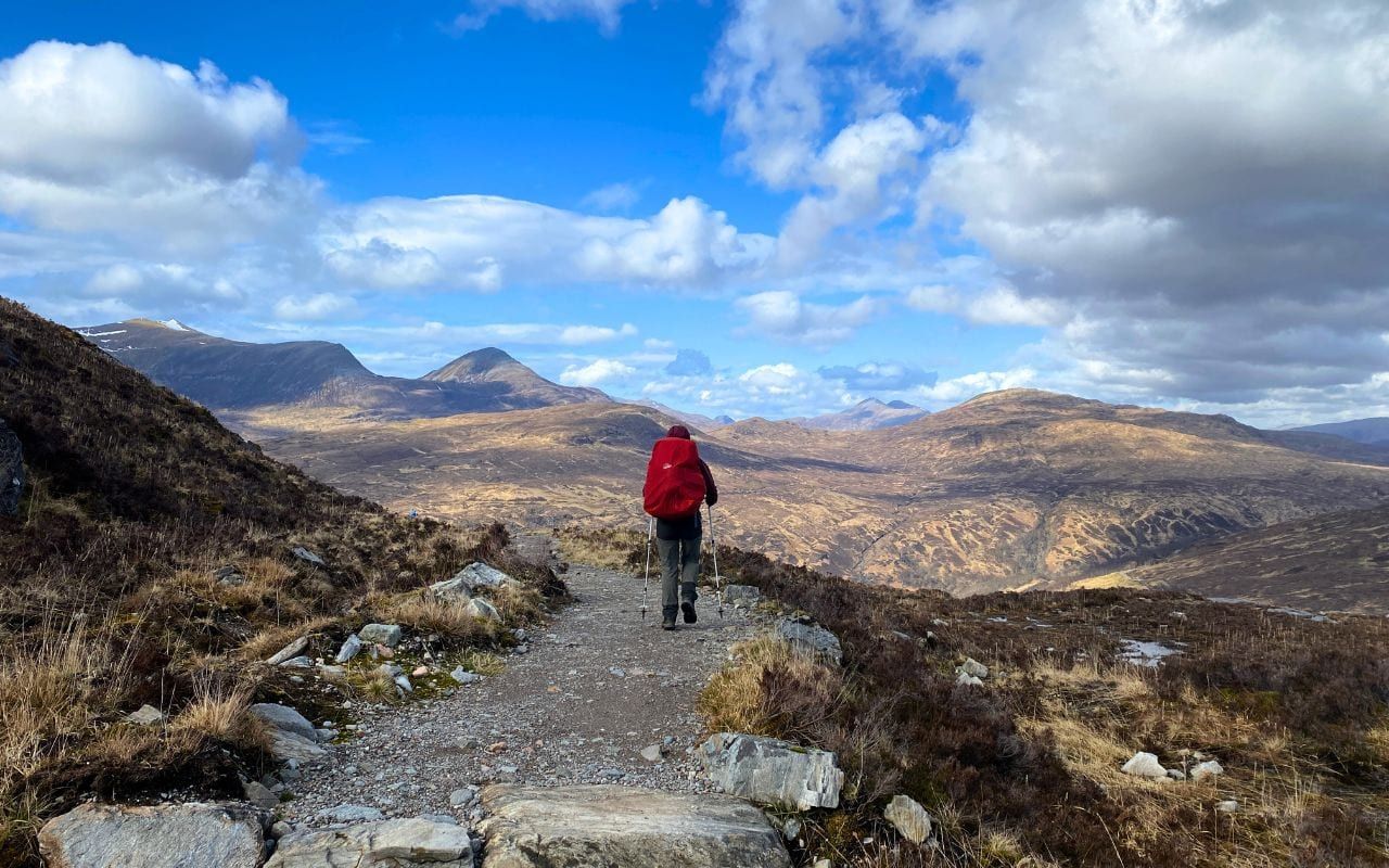 Walker on a Highland trail overlooking vast mountain scenery on the West Highland Way.