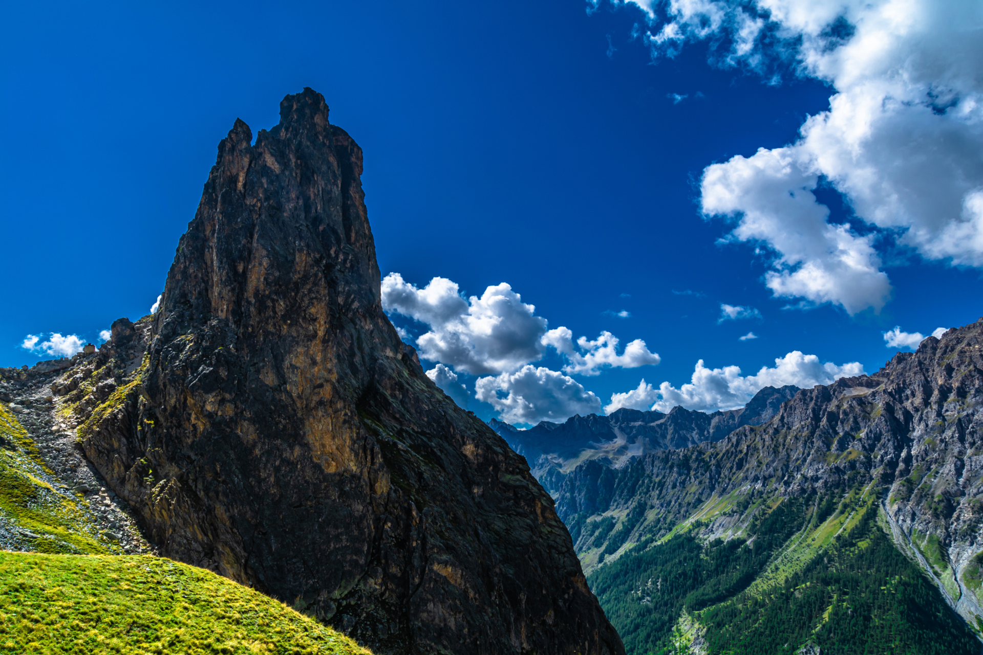 Rocca Provenzale rising above grassy slopes and rugged mountain peaks in Val Maira.
