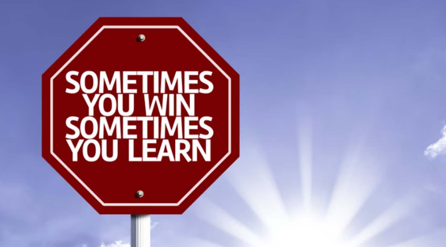 A red stop sign reading 'Sometimes you win, sometimes you learn' against a bright sky