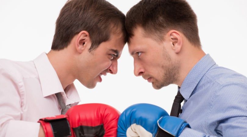 Two businessmen in boxing gloves squaring up head to head