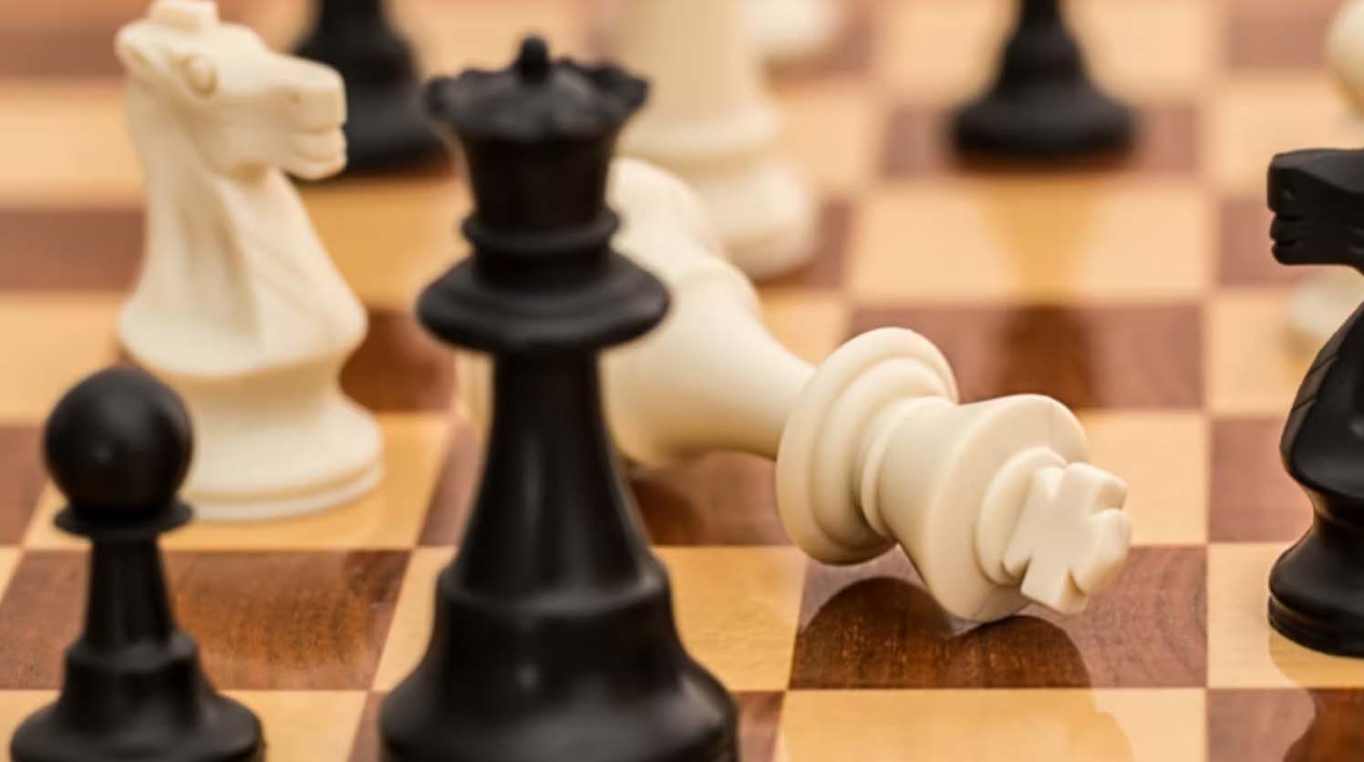 A chessboard with a toppled white king beside a standing black queen
