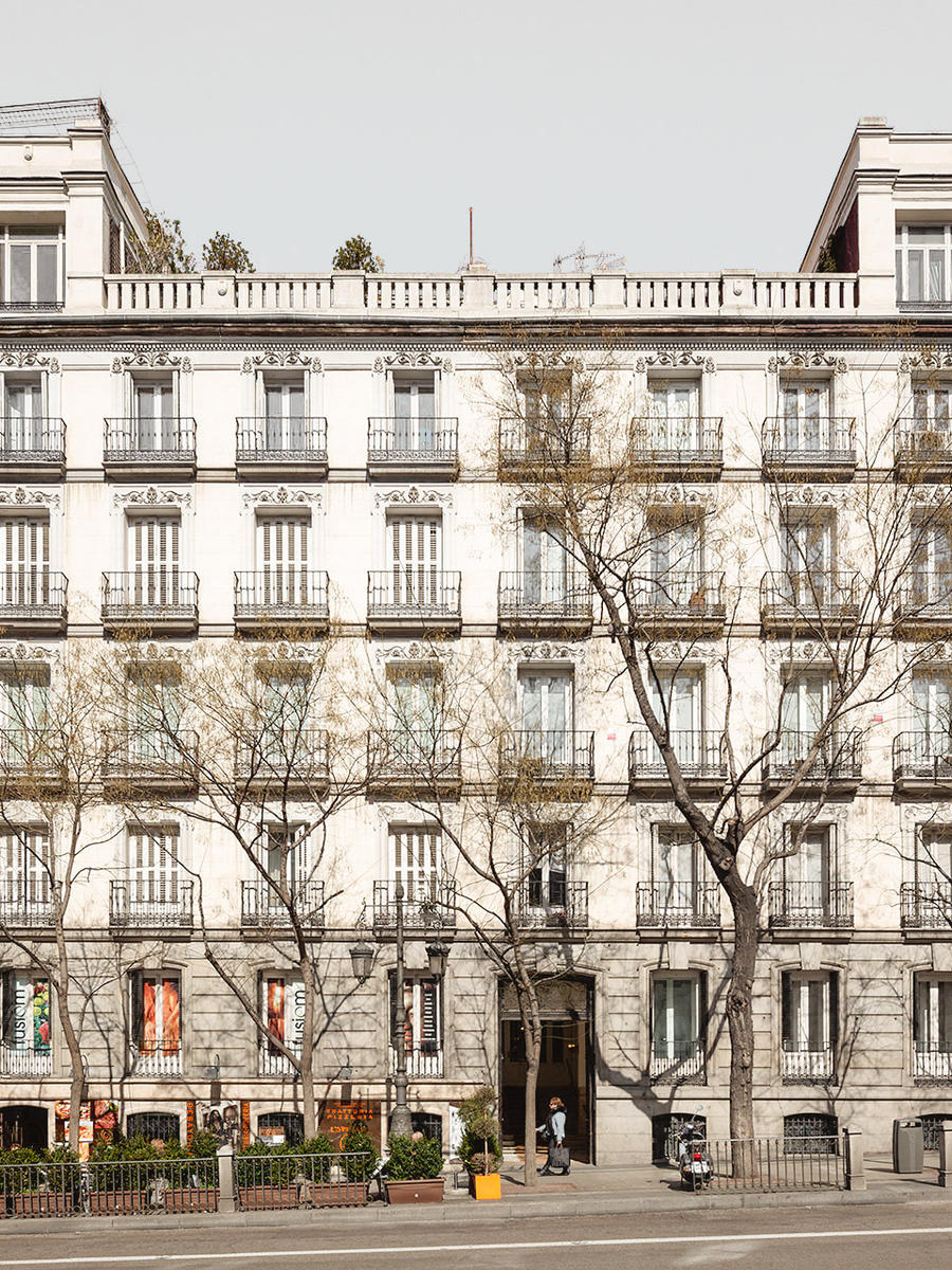 Fachada clásica de edificio residencial con balcones y árboles al frente.