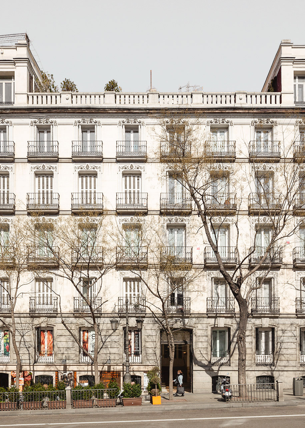 Fachada clásica de edificio residencial con balcones y árboles al frente.