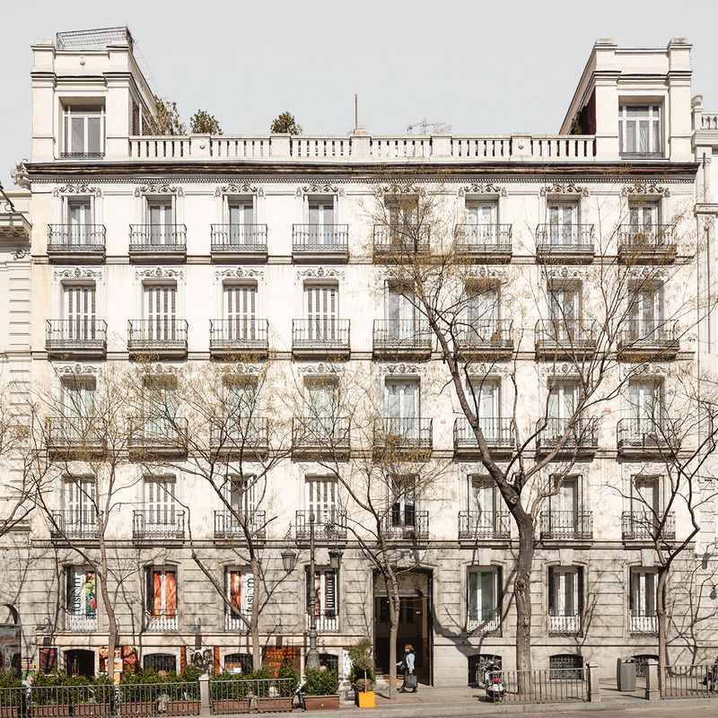 Fachada clásica de edificio residencial con balcones y árboles al frente.