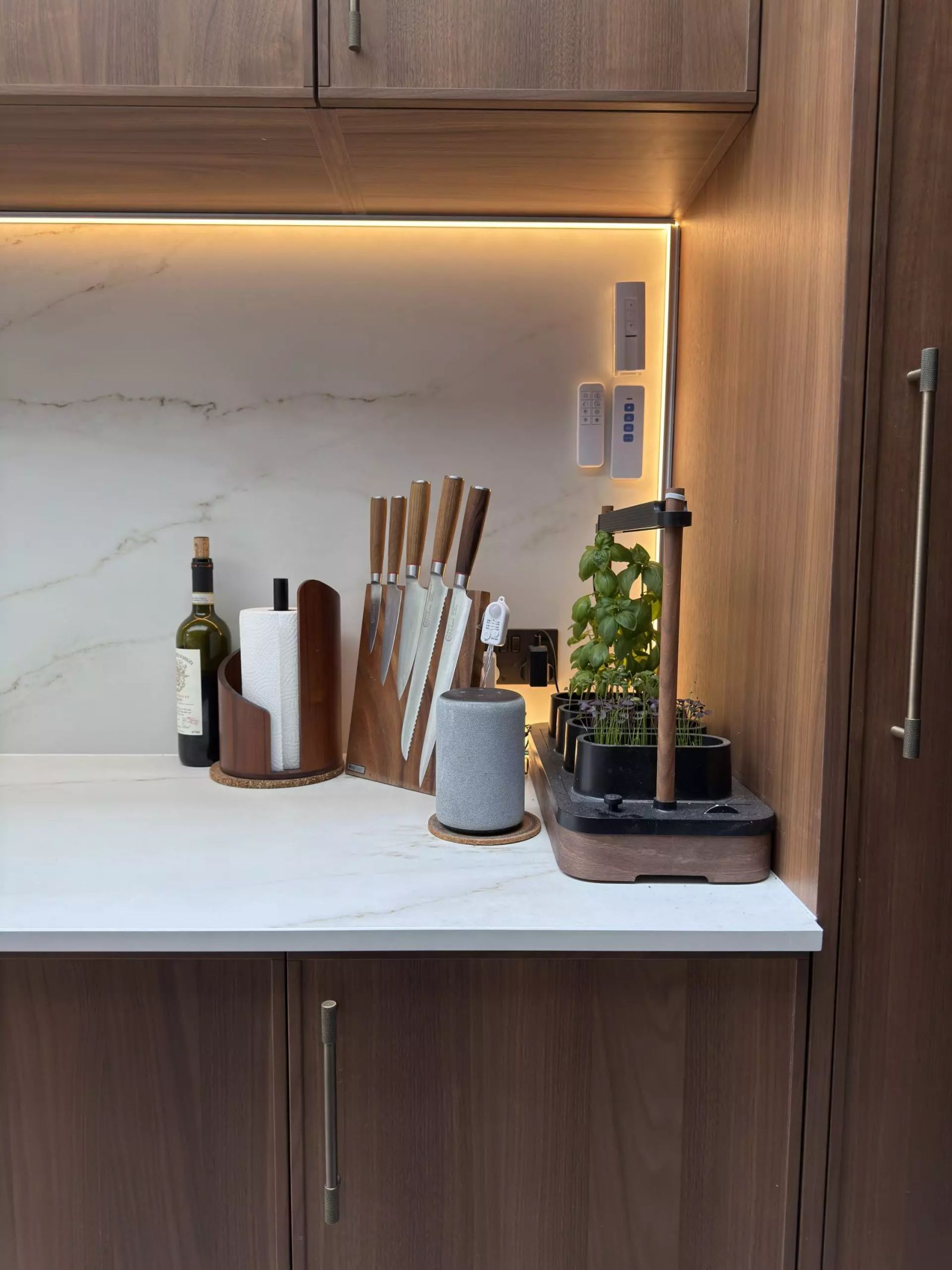 Close-up of a kitchen worktop and marble splashback, with a knife block and countertop herb garden