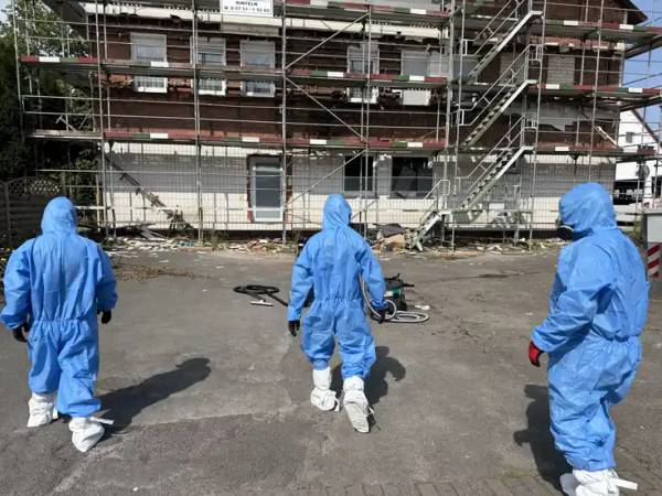 Drei Mitarbeiter in Schutzanzügen vor dem eingerüsteten Wohngebäude in Hessisch Oldendorf mit asbestbelasteter Fläche davor