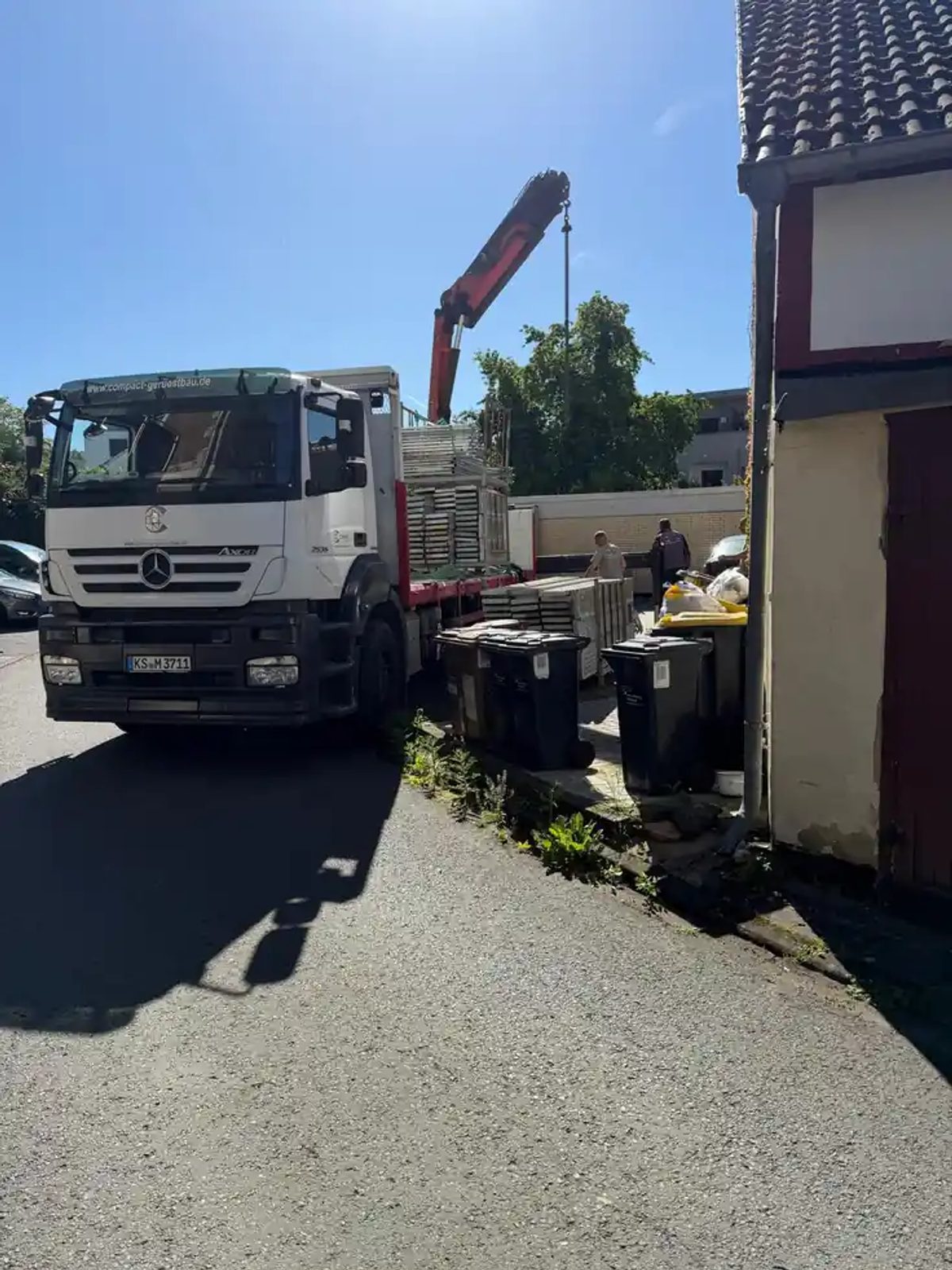 Kranfahrzeug hebt Gerüstbauteile über die enge Hofzufahrt in Kaufungen ein