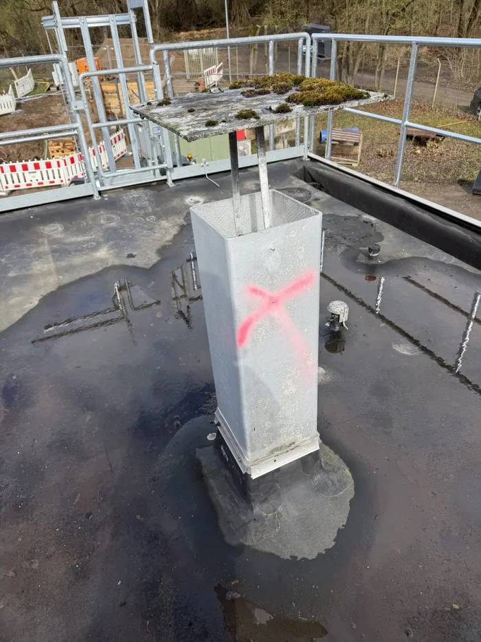 TRGS 519: mit Kreuz markierter Schacht auf einem Flachdach, abgesperrt mit Bauzaun und Absperrband