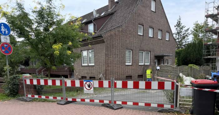 Asbest-Abriss in der Nachbarschaft: abgesperrte Baustelle in einer Wohnstraße mit Warnschild Asbestfasern vor dem Wohnhaus