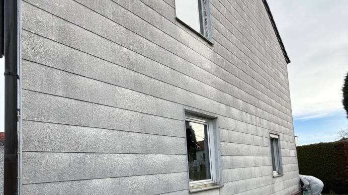 Asbest überstreichen ist verboten: verwitterte graue Faserzement-Fassadenplatten an einem Wohnhaus.