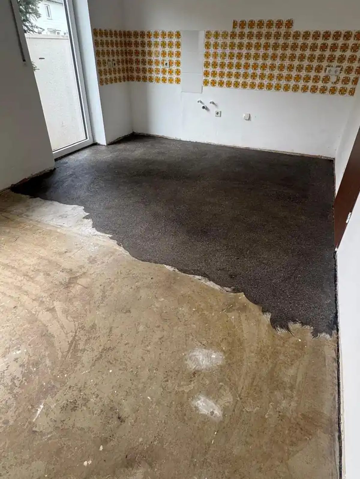 Teilweise abgeschliffene Fläche in Hof: hinten die dunkle Kleberschicht, vorne der bereits freigelegte mineralische Untergrund.