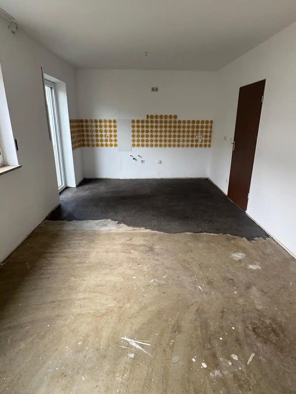 Wohnraum in Hof während des Kleberabtrags: vorne der geschliffene Untergrund, hinten die noch dunkle Restfläche unter dem ehemaligen PVC.