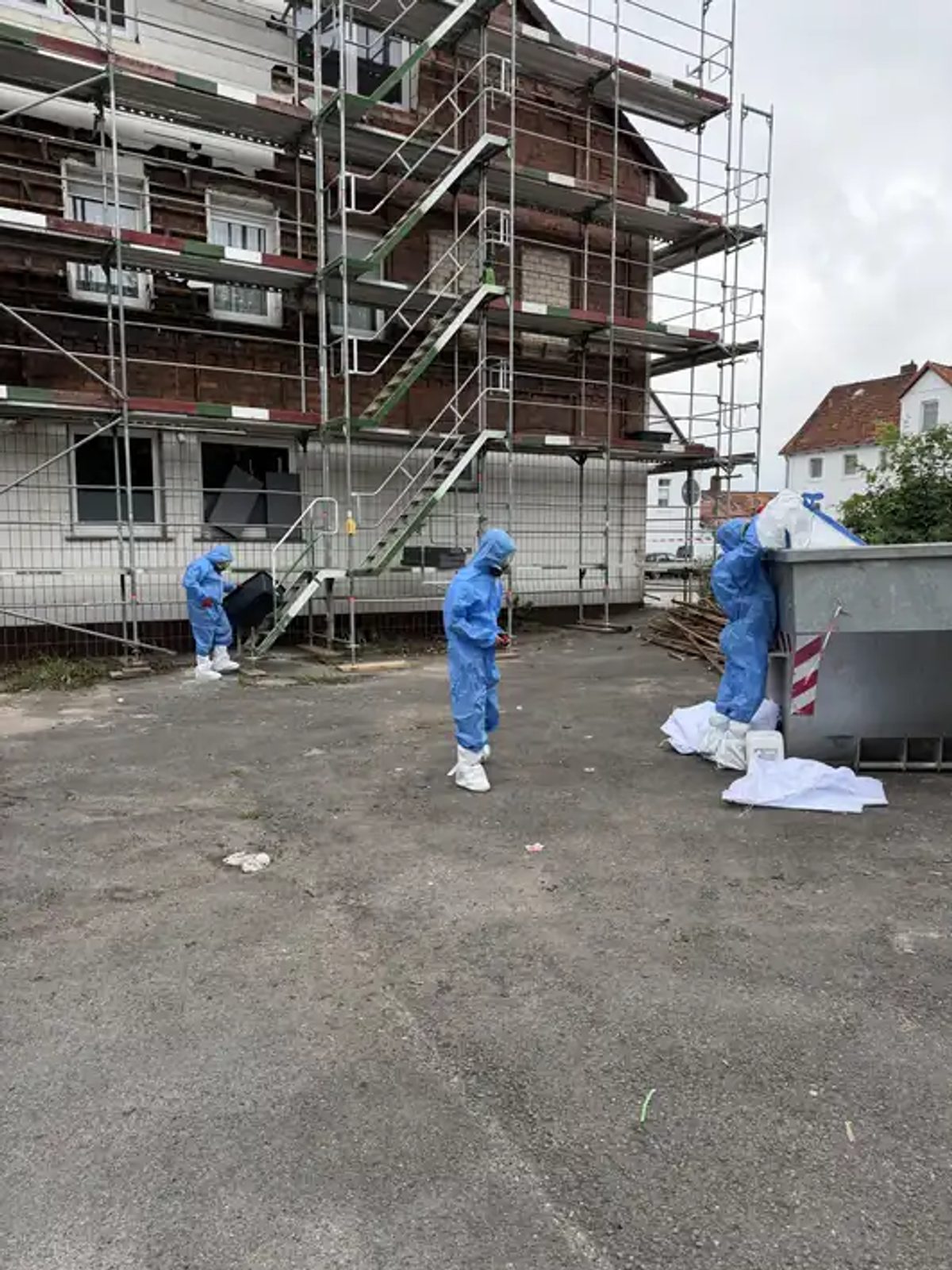 Mitarbeiter in Schutzanzügen nehmen Asbestreste auf dem Gerüst an der Außenfassade in Hessisch Oldendorf händisch auf