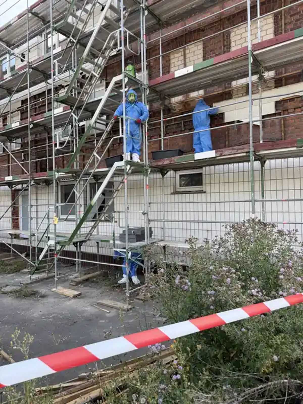 Verpacken der aufgenommenen Asbestreste in Gewebesäcke am Absetzcontainer neben dem eingerüsteten Gebäude in Hessisch Oldendorf