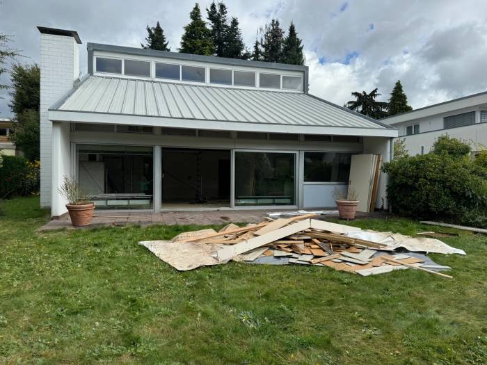 Flachdachhaus mit Rückbaumaterial auf der Rasenfläche – Kostenfaktoren, Förderung und Steuervorteile bei der Asbestsanierung