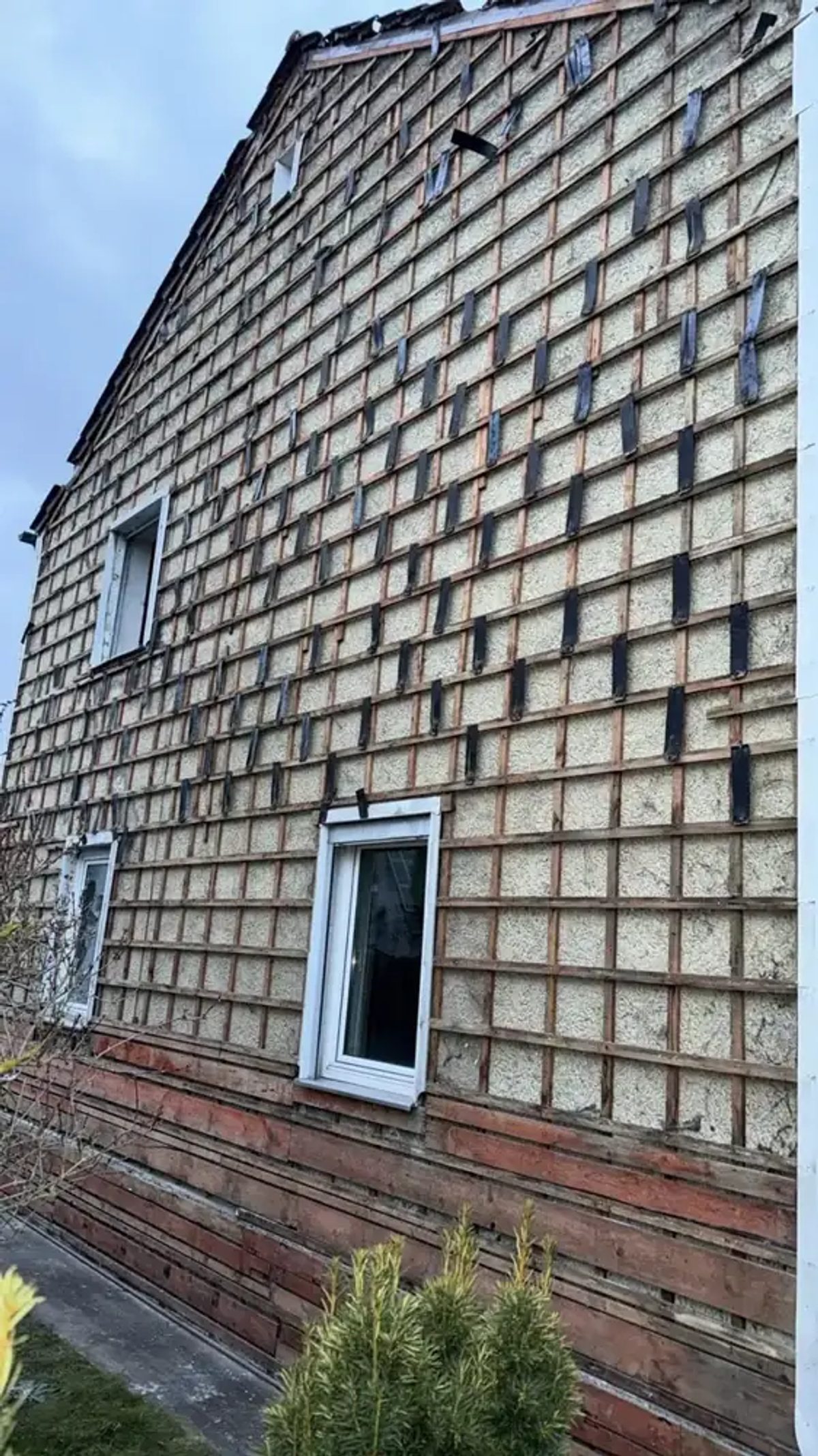 Teilweise abgenommene Asbestschindeln an einer Hausfassade, dahinter die Lattung – Rückbau nach TRGS 519.