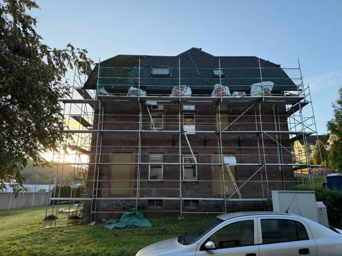 Wann wurde Asbest verbaut – eingerüstetes älteres Mehrfamilienhaus, dessen Dach bis auf die Lattung abgedeckt ist