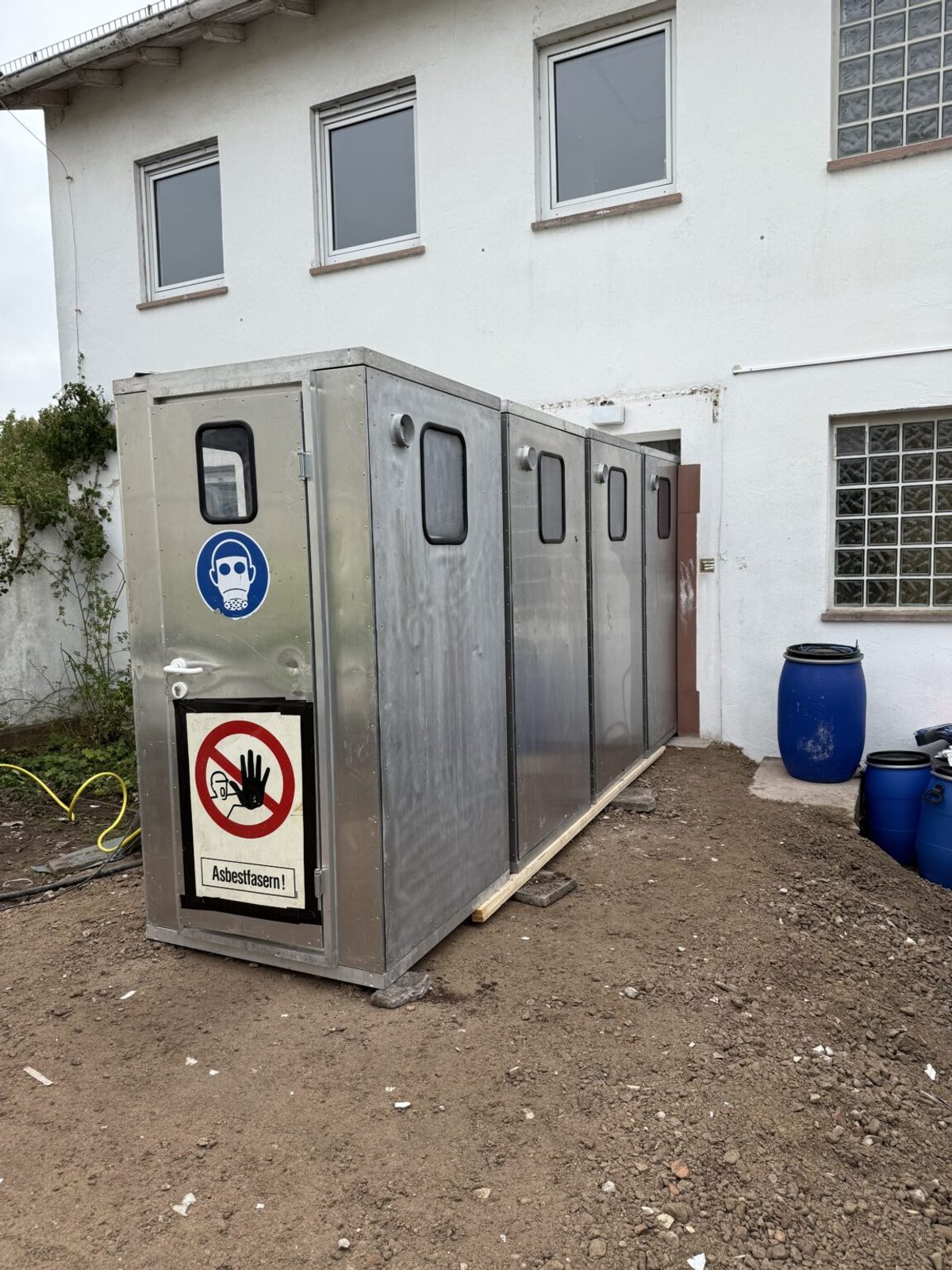 Personenschleuse mit Atemschutz-Gebotszeichen und Warnschild Asbestfasern an einer abgesperrten Baustelle