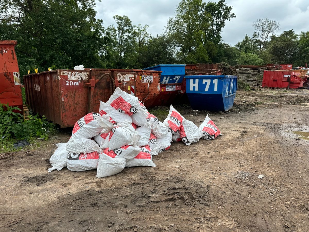Verschlossene Entsorgungssäcke mit rotem Warnaufdruck vor Absetzcontainern auf einem Entsorgungsplatz nach dem Rückbau einer Fassadenverkleidung