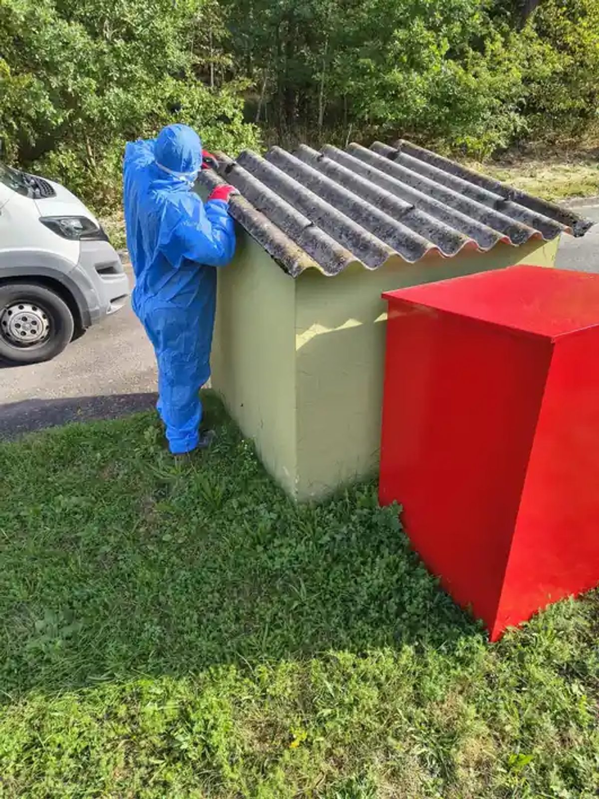 Mitarbeiter im Schutzanzug nimmt die Asbestzement-Wellplatten einzeln vom Dach eines Nebengebäudes im Tanklager Aschaffenburg ab