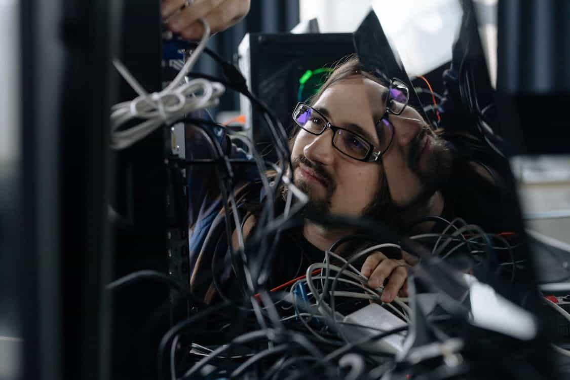 employee working through the tangle of cables behind the computer