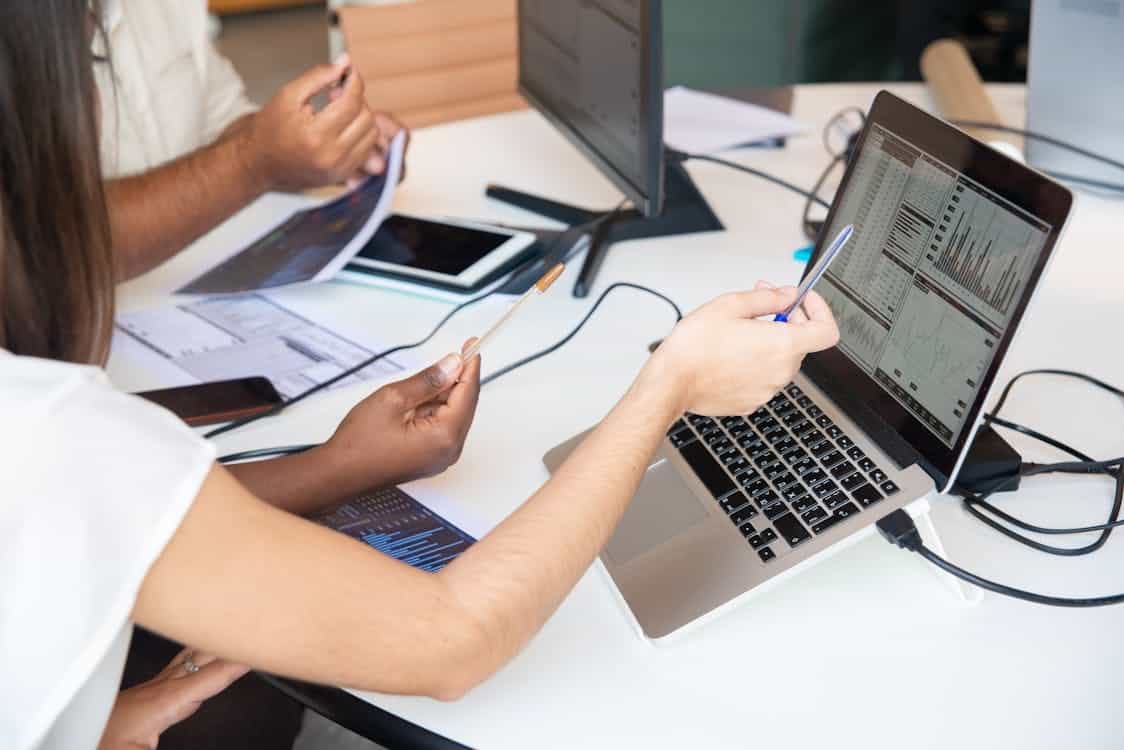 peoples hands pointing to a laptop with charts