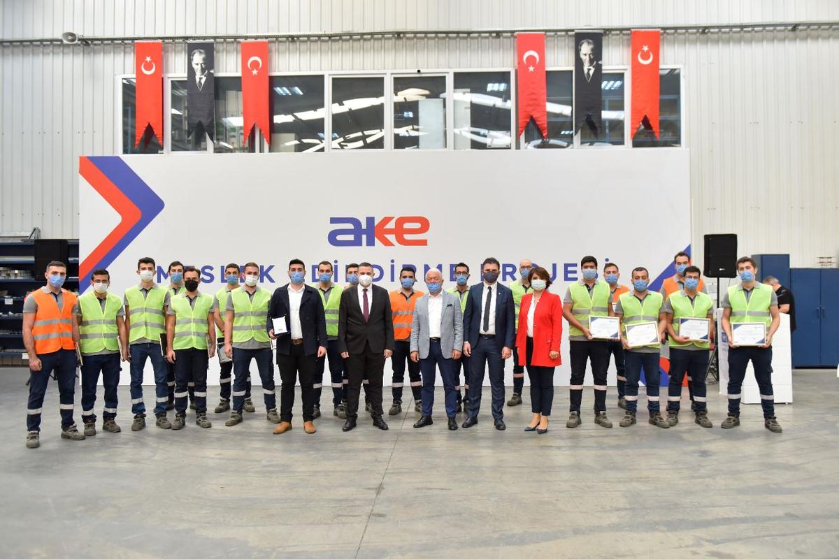 Sertifikalarını alan AKE çalışanları şirket logosu önünde toplu halde