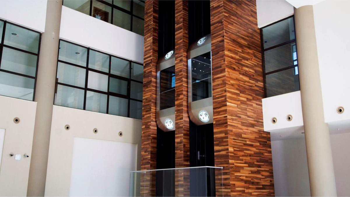 Modern atriumda ahşap kaplamalı şaftta iki panoramik cam asansör