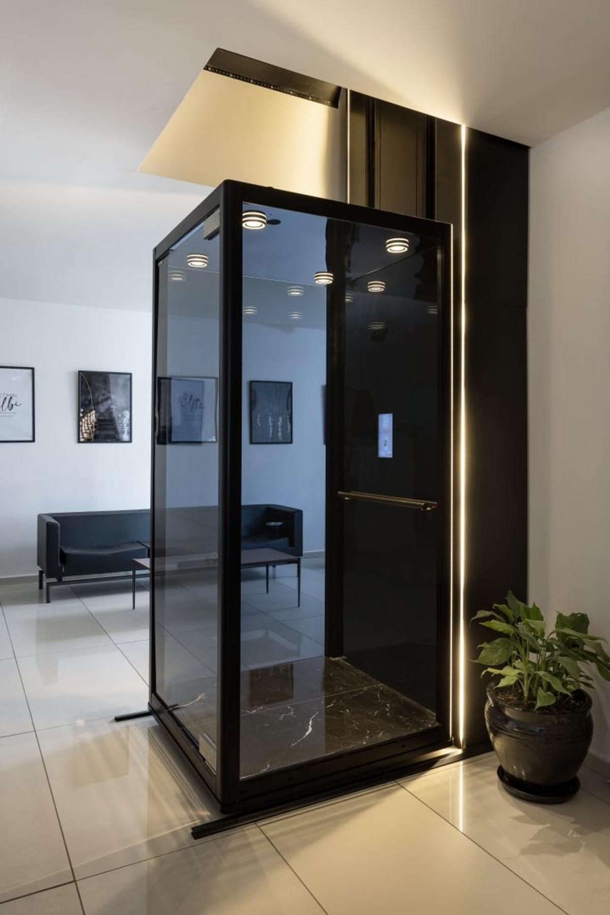 Freestanding black glass home lift in a bright living room