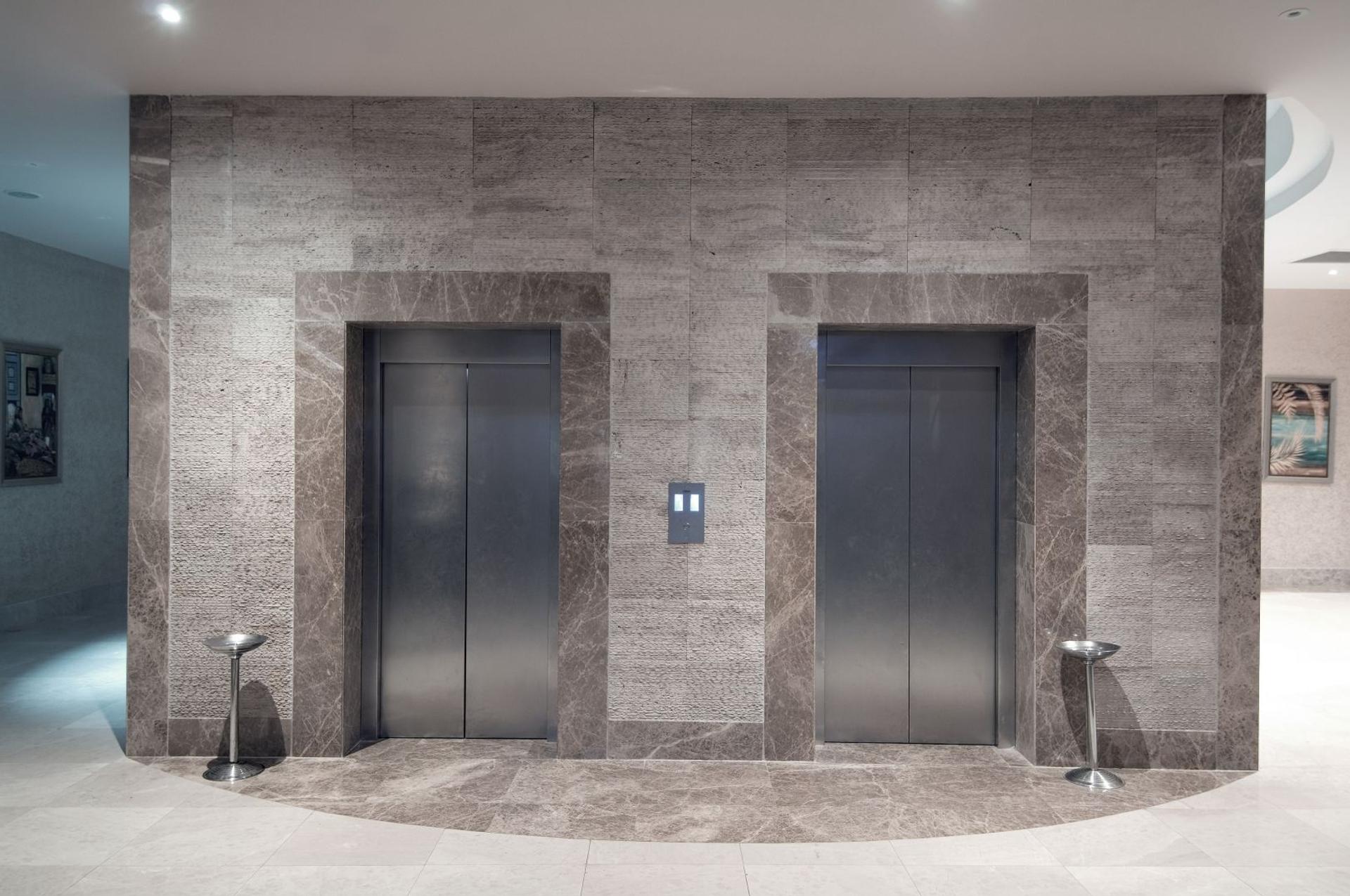 Two stainless steel elevator doors in an elegant marble-clad residential lobby