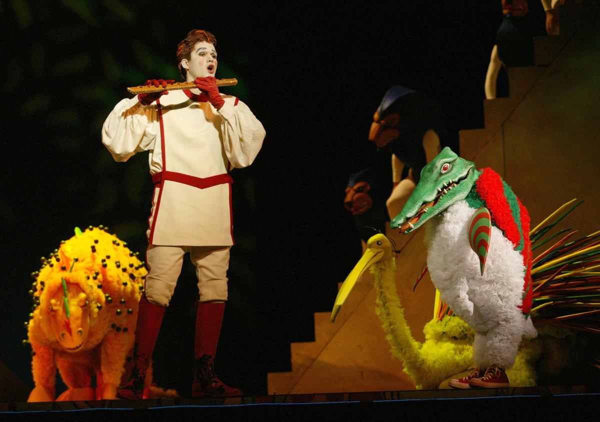 Un chanteur incarnant Tamino avec une flûte, à côté de créatures fantastiques sur la scène de La Flûte enchantée