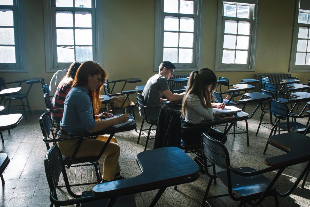 Grupo de estudiantes sentados en pupitres individuales realizando una prueba escrita