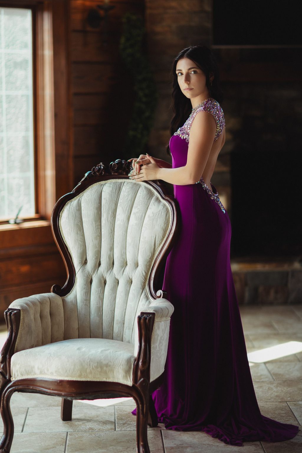 Model in a deep purple gown standing behind an ornate white throne chair.