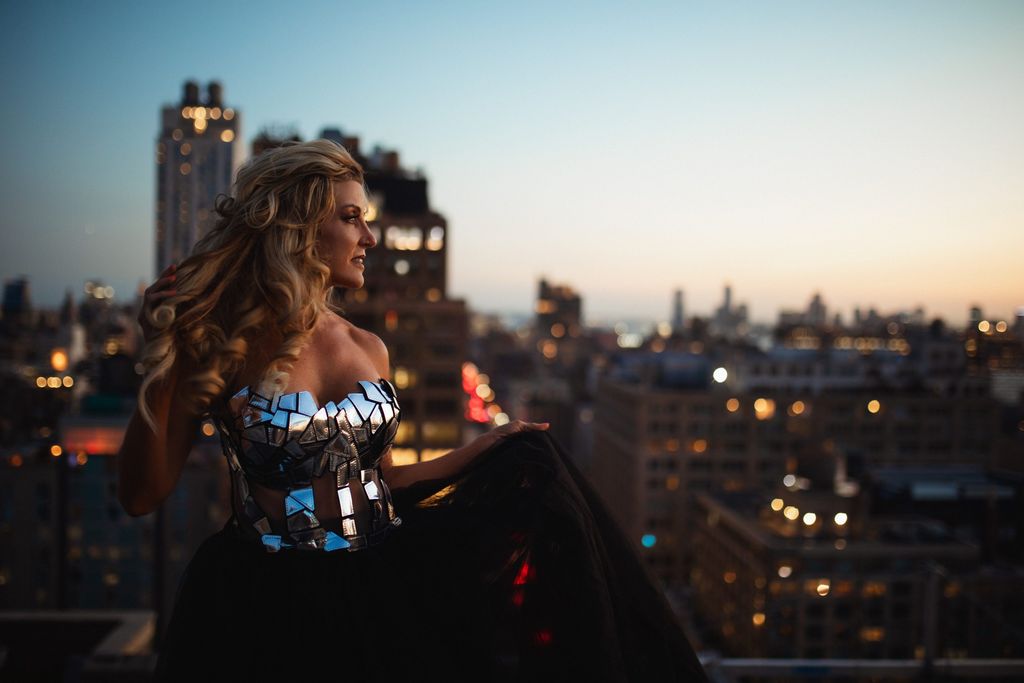 Model in a sequined bodice and dark skirt on a rooftop at night with the lit city skyline behind.