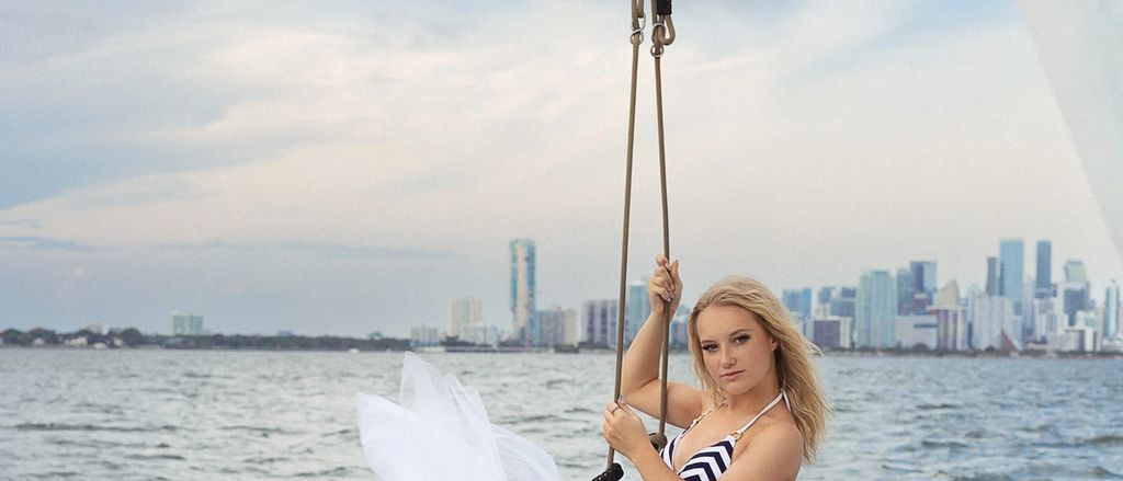Model in a white tulle skirt on a rope swing over the water, the Miami skyline in the distance.