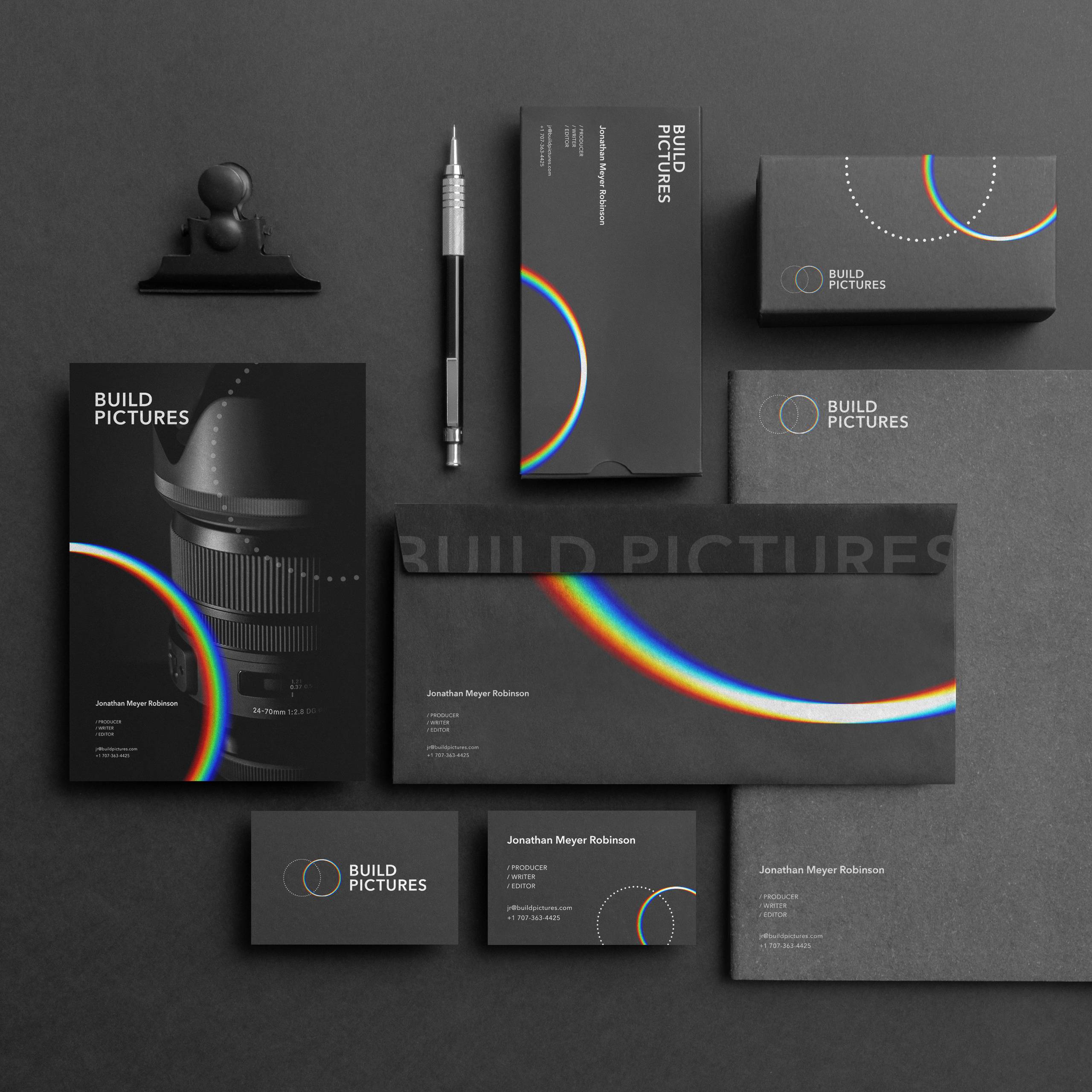 Build Pictures stationery suite with black cards, envelopes, folders, and circular rainbow graphics.
