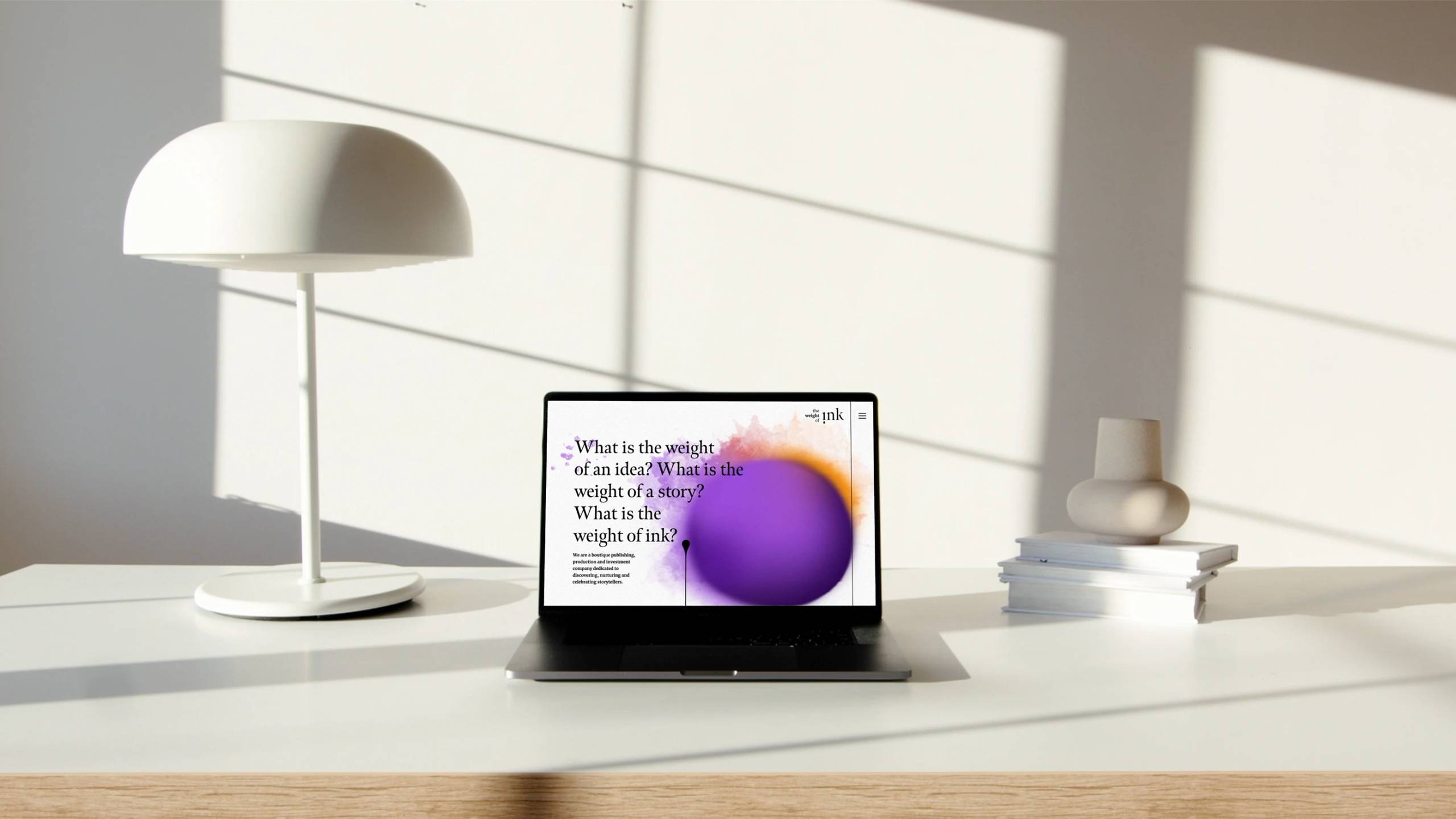 The Weight of Ink website shown on a laptop in a light interior.