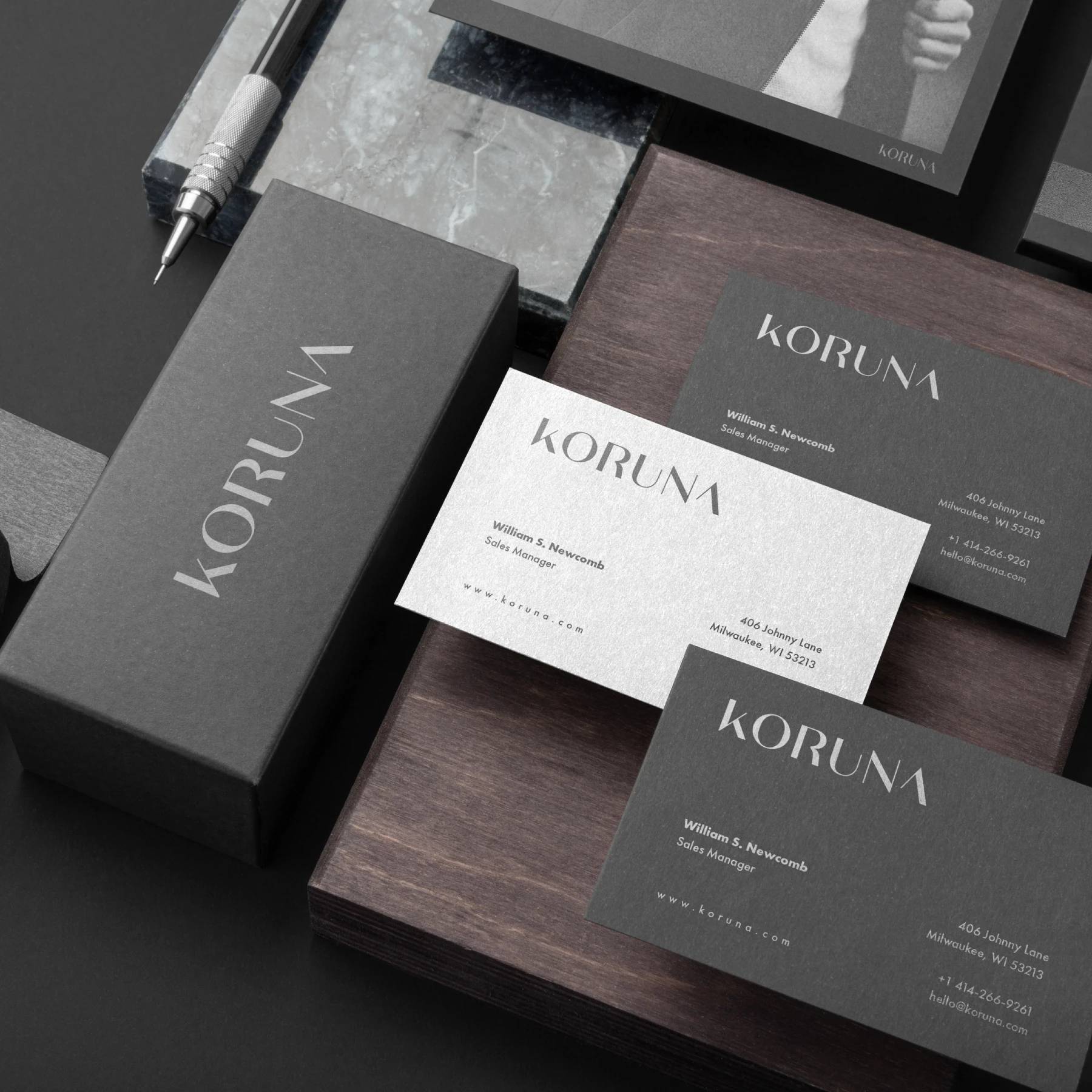 Koruna black and white business cards and packaging arranged on dark wood.