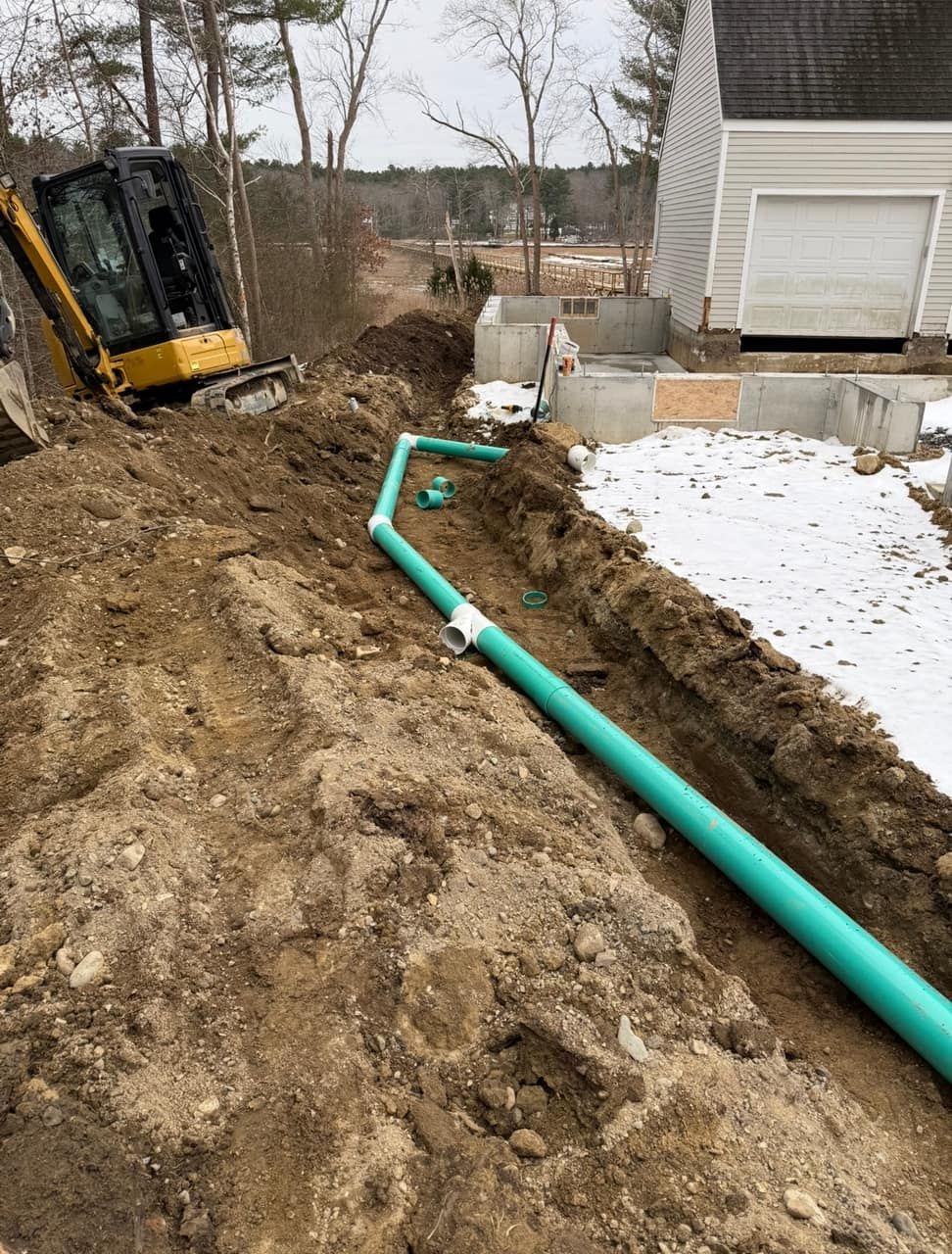 Drainage pipe runs bedded in gravel during a residential drainage installation Legacy Excavation is a Title 5 excavation contractor that installs French drains and storm-water drainage across Plymouth County, MA