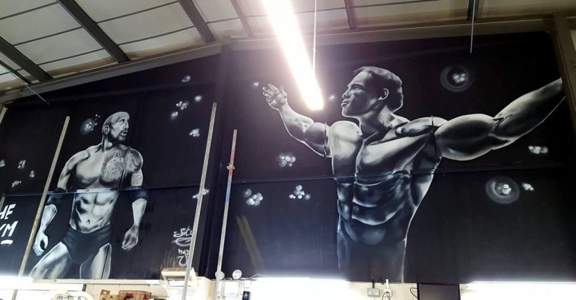Large black and grey gym wall mural with photo-realistic bodybuilder portraits, commercial graffiti for a fitness centre by Thomas Palaniuk
