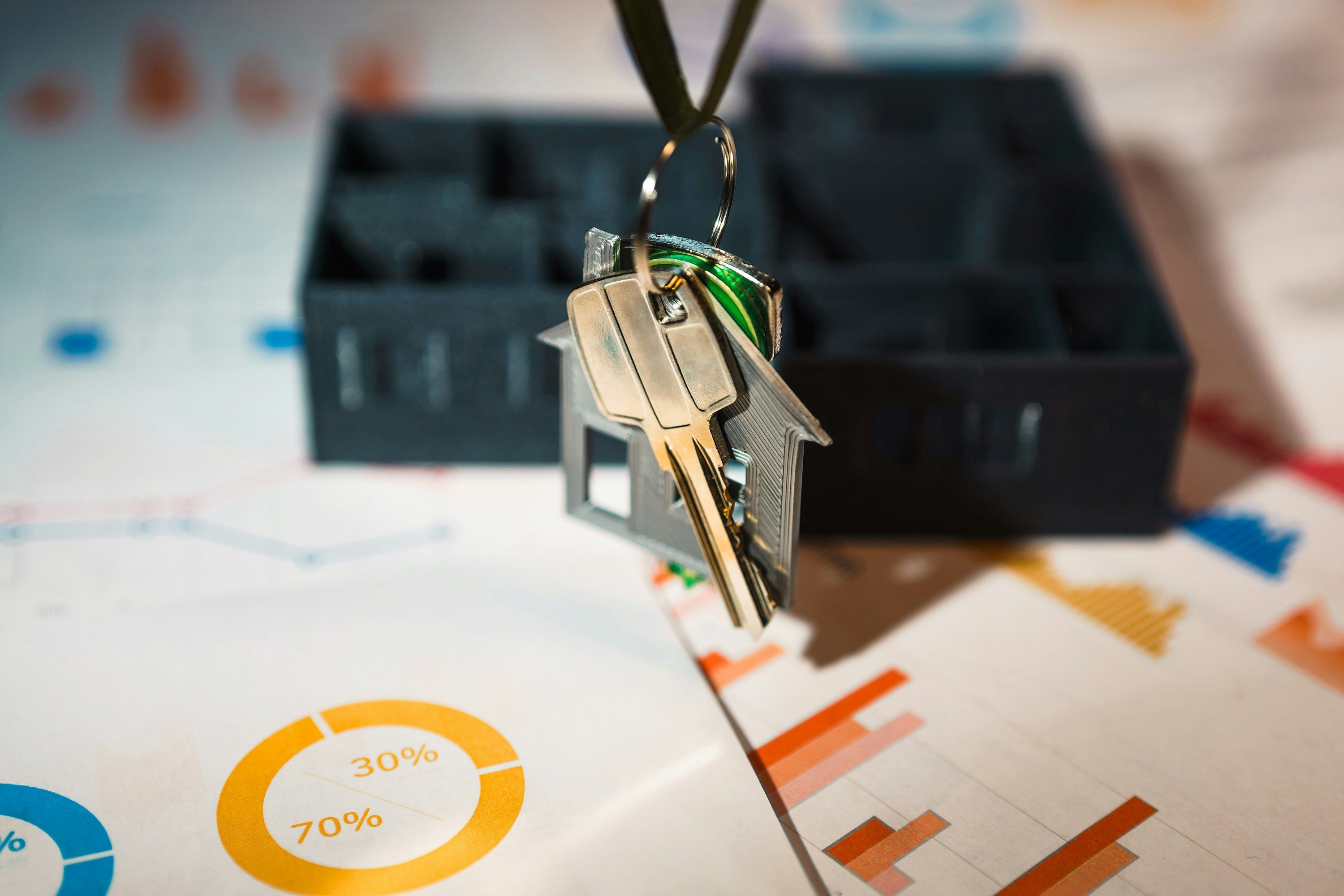 A house-shaped keyring holding keys, hanging above financial charts including a donut chart split 70 percent to 30 percent