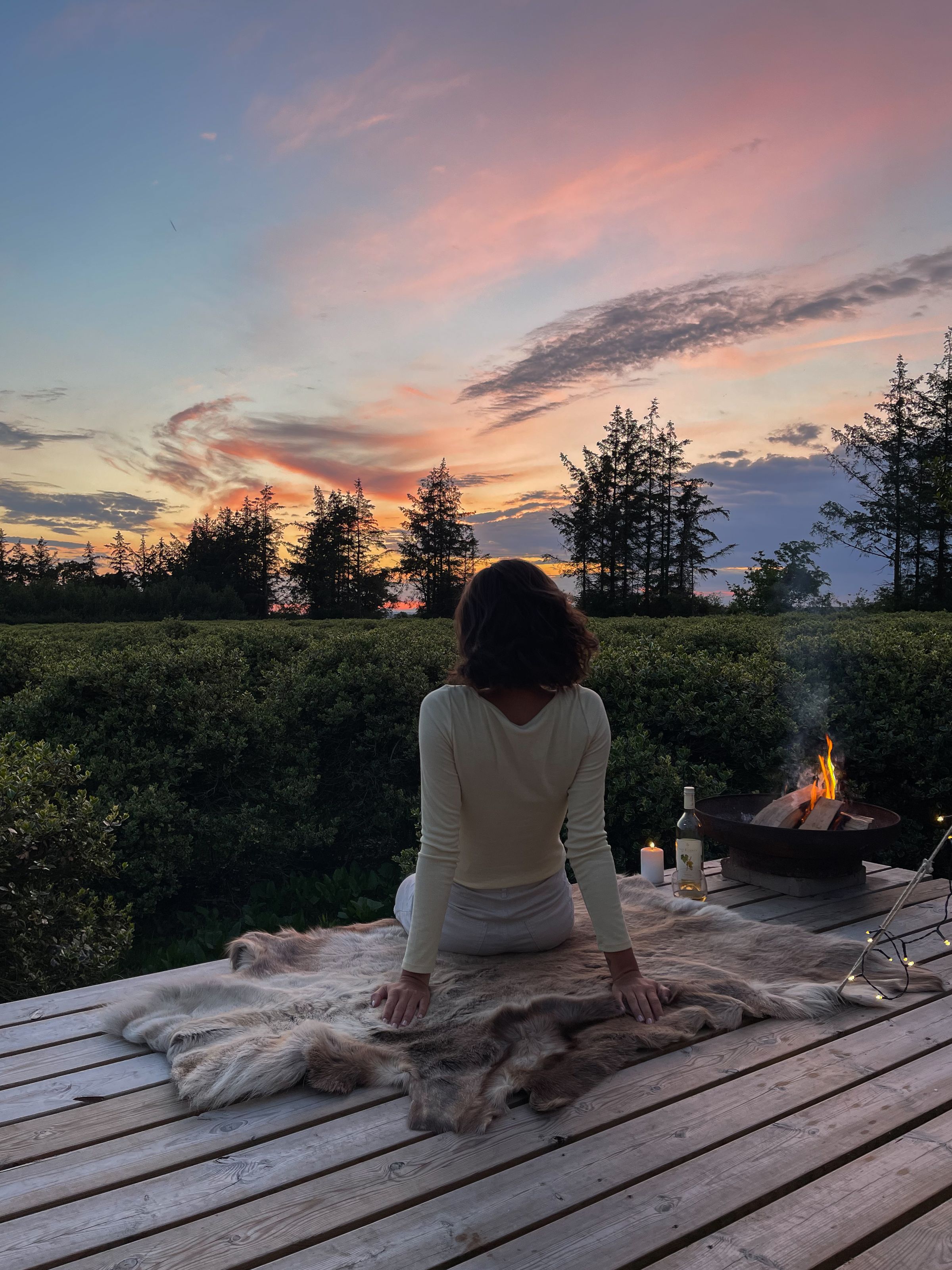 Romantisk ophold i naturen med kvinde på terrasse, bål og smuk solnedgangshimmel