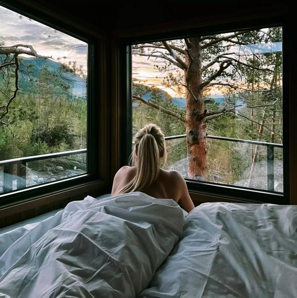 En tjej njuter av utsikten från sin säng i en trädkoja i Norge