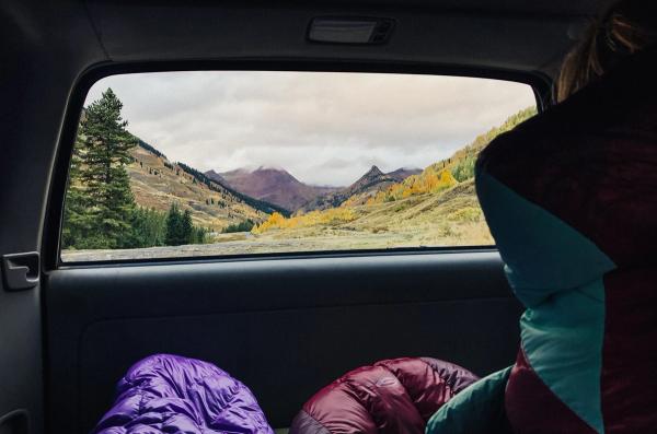 Person in a sleeping bag in a car, looking at nature