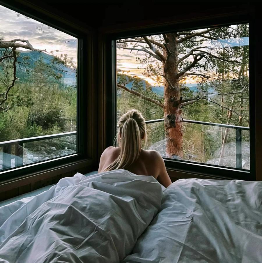 Jente som ser på utsikten fra sengen av en tretopphytte på østlandet